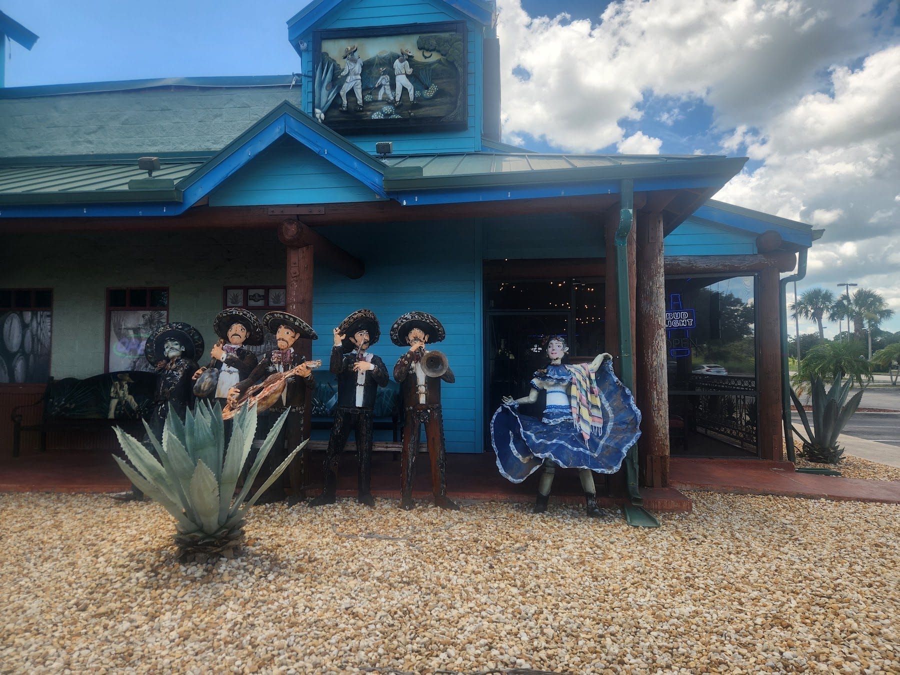 The hand-carved mariachi band and dancer stand against the turquoise siding of Azul Tequila in Sebring in full daylight